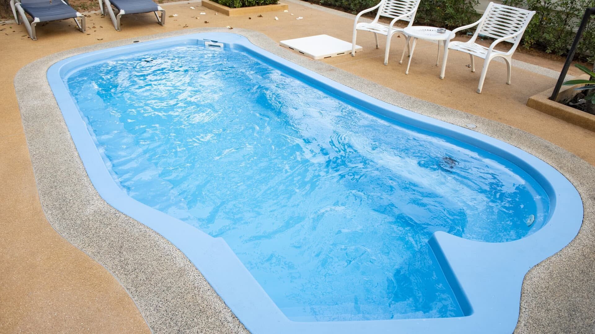 Backyard swimming pool with blue water, tan deck, lounge chairs, and white patio chairs