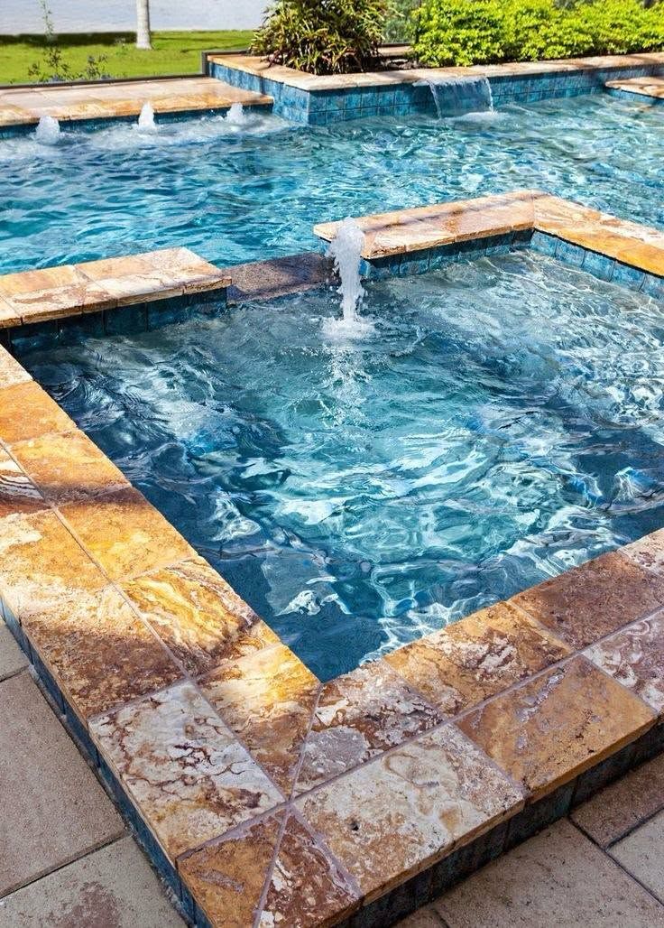 Small blue tiled pool with water jets and stone edging in an outdoor spa area
