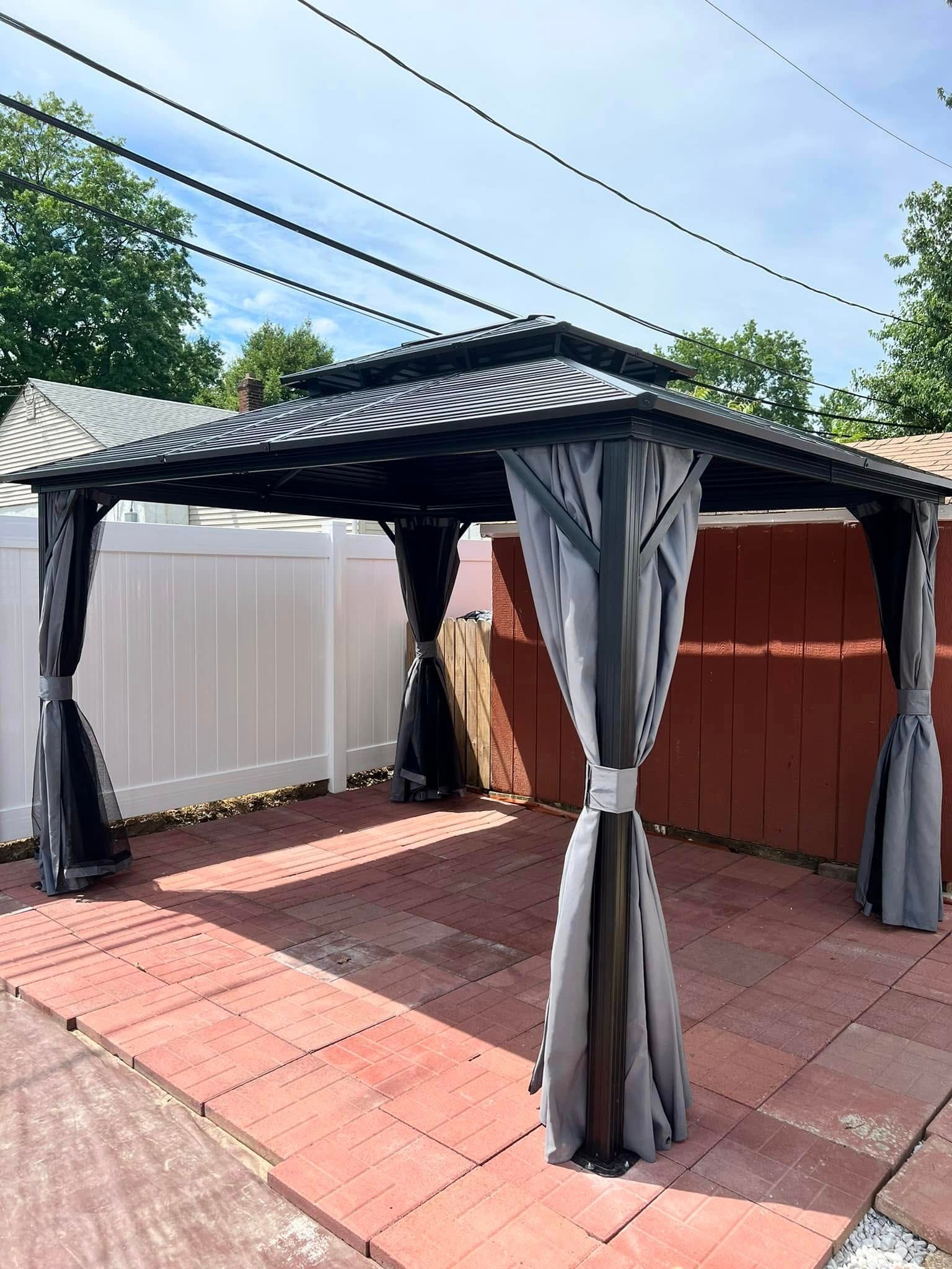 Gray gazebo with curtains on a red brick patio in a fenced backyard
