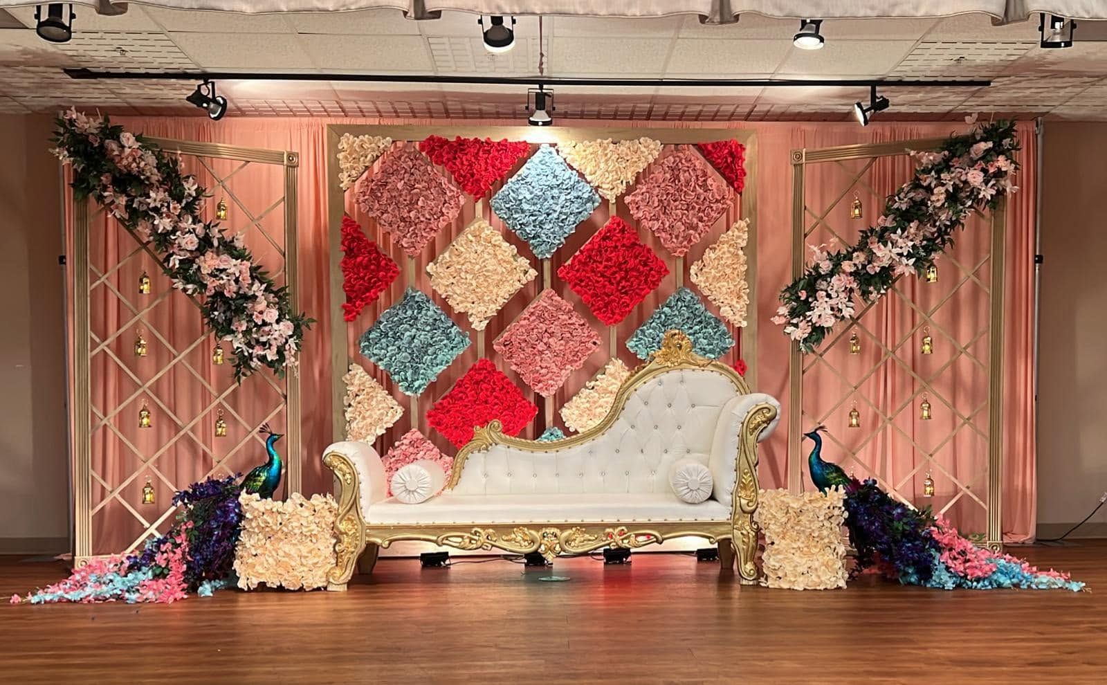 Elegant event stage with white tufted sofa, colorful diamond backdrop, and floral arrangements