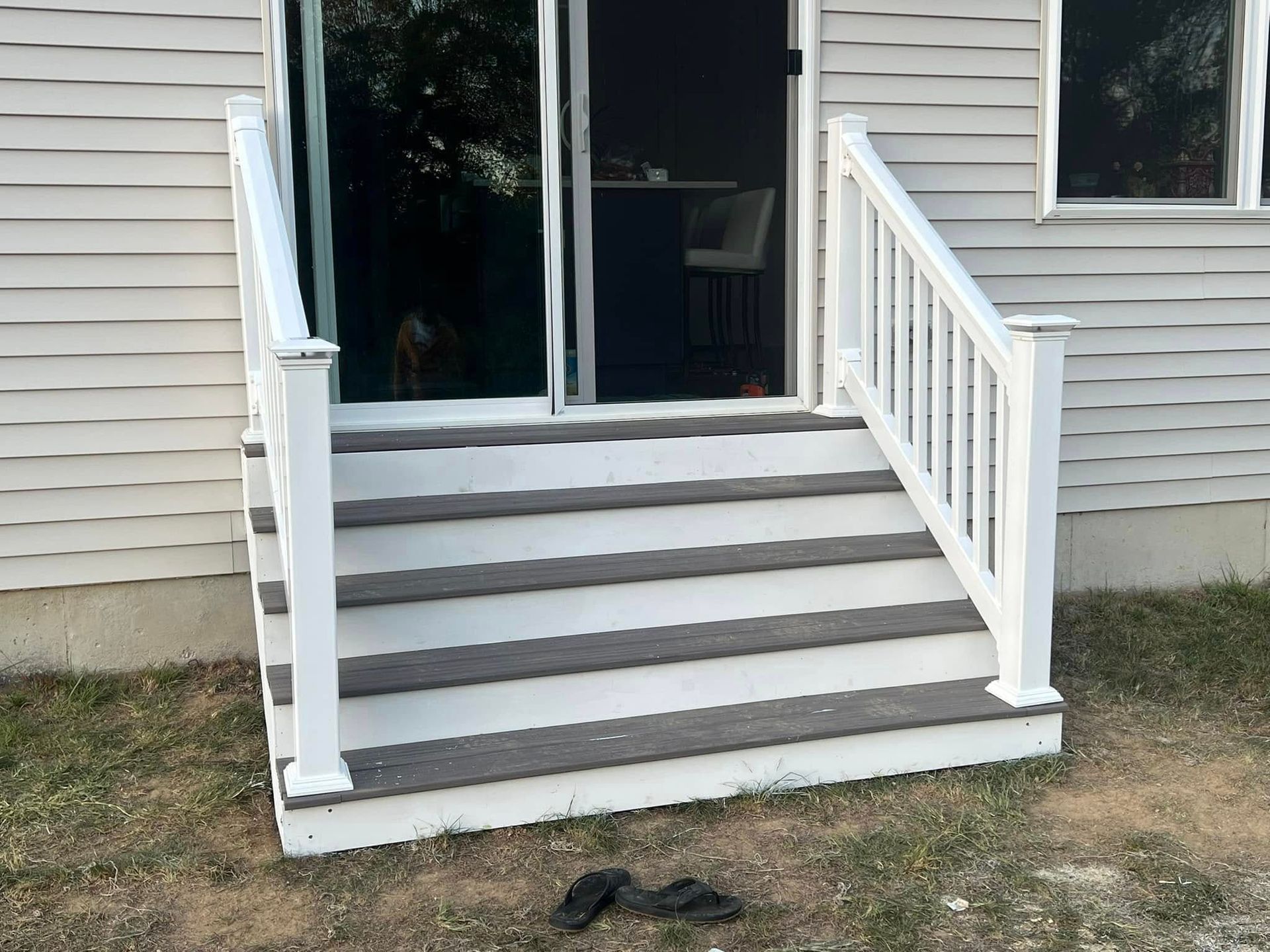 Front steps with white railings leading to a sliding glass door on a house.