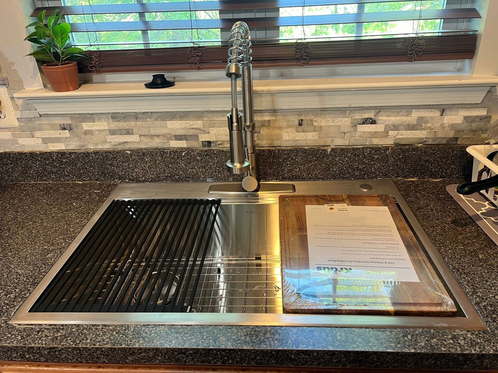 Kitchen sink with stainless steel basin, tall faucet, and drying rack by a window.