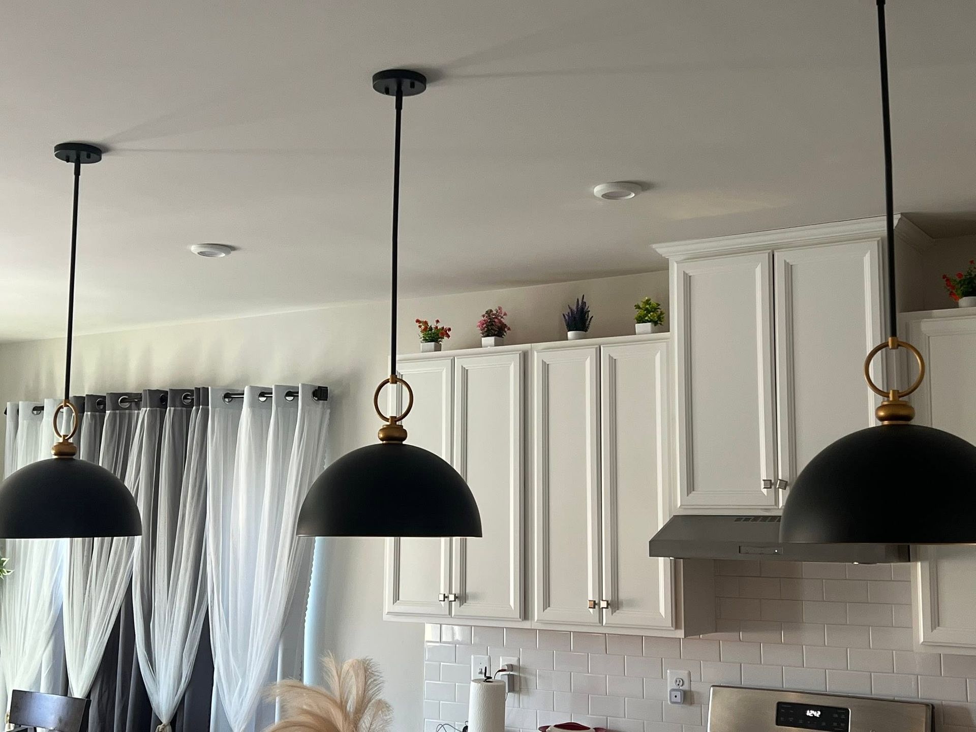 Modern kitchen with white cabinets, black pendant lights, and gray curtains by a window