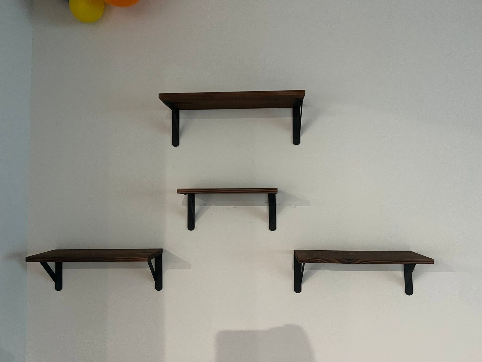 Five small wooden wall shelves mounted in a staggered pattern on a white wall.