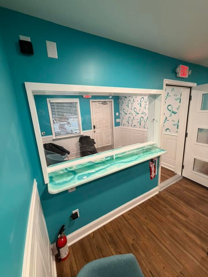 Teal hallway wall with a service window, white trim, wood floor, and doors in a bright indoor space
