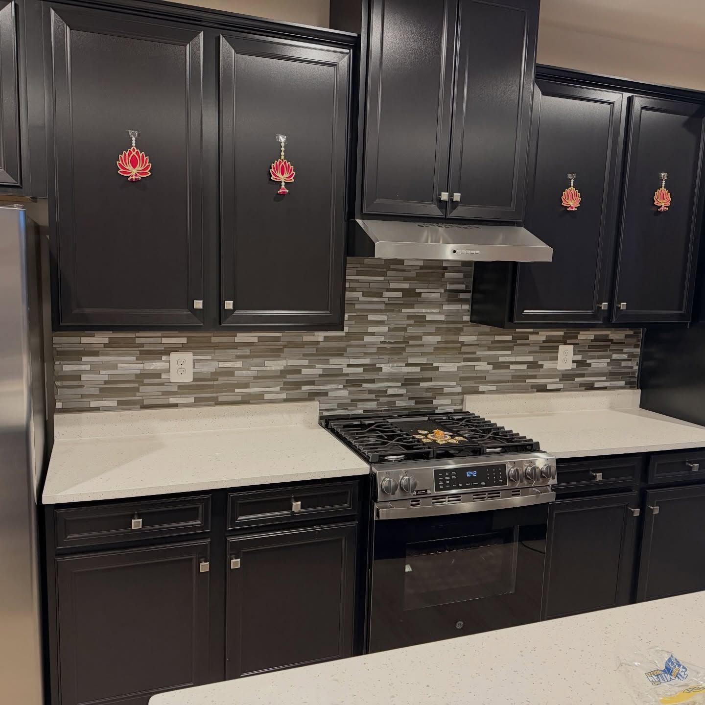 Modern kitchen with black cabinets, white countertops, gray tile backsplash, and stainless steel stove.