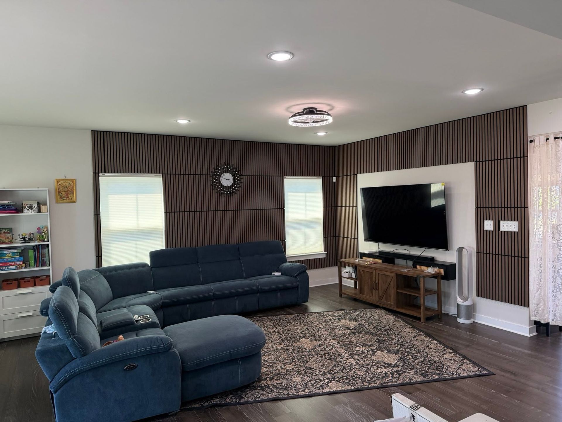 Spacious living room with blue sectional sofa, TV, patterned rug, and striped curtains