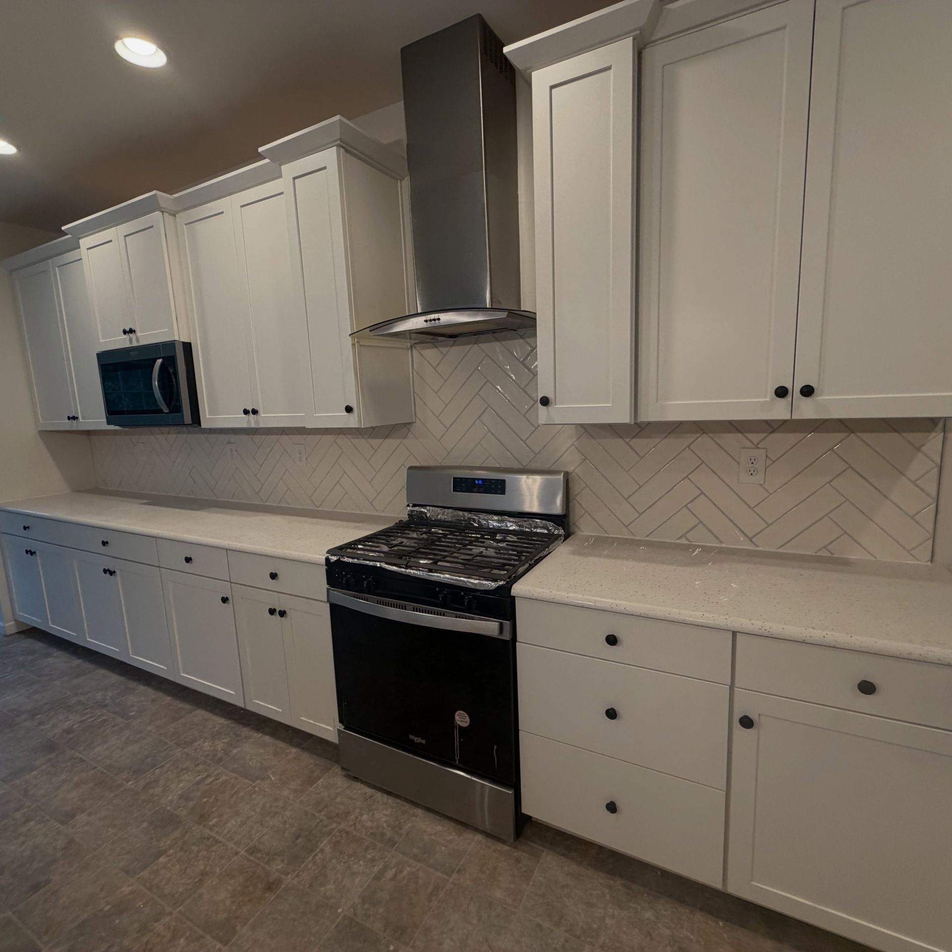 Modern white kitchen with black stove, stainless hood, white cabinets, and tiled backsplash