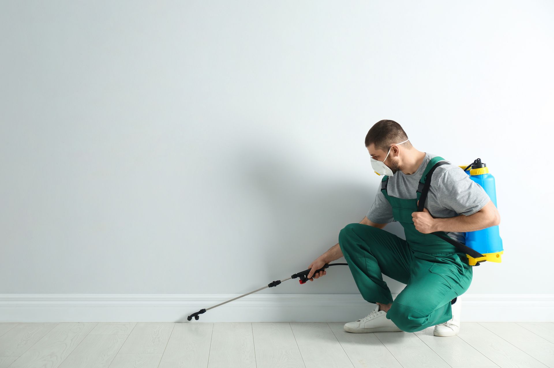 Pest control worker in uniform spraying pesticide indoors. Pest control worker in uniform spraying pesticide indoors.