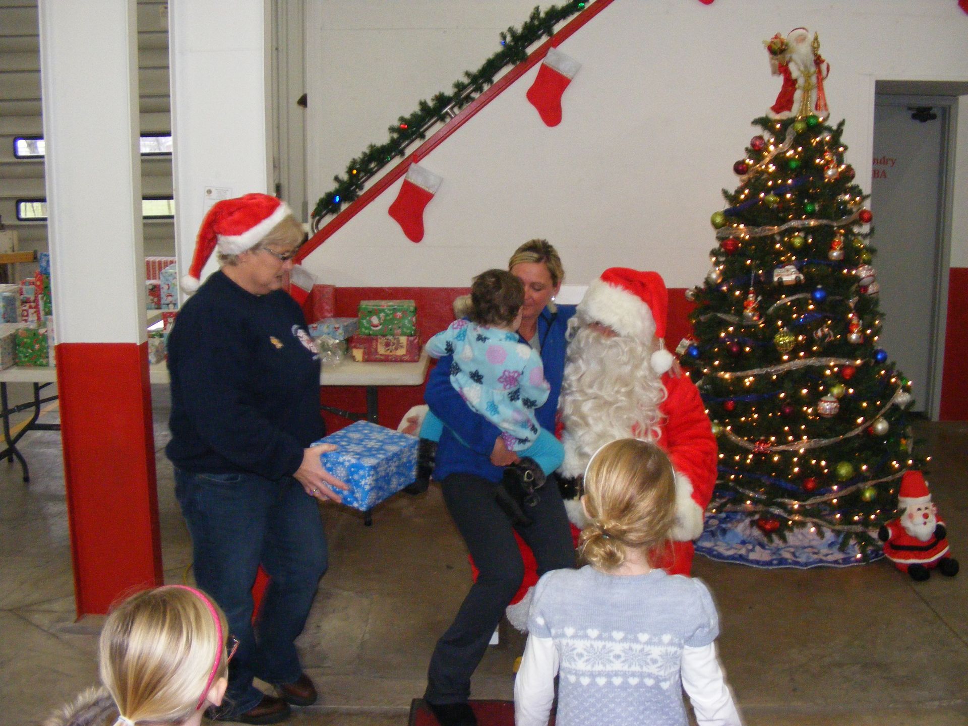 Santa Claus with children at a holiday event. Gifts and Christmas tree in decorated room.