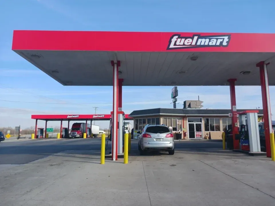 Fuelmart gas station with red canopy, cars fueling, and building in the background.