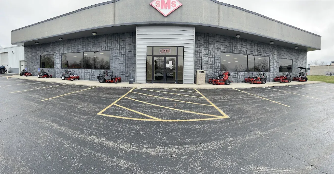 Building with stone facade, SM logo, entrance, and lawnmowers displayed outside on a wet, gray day.