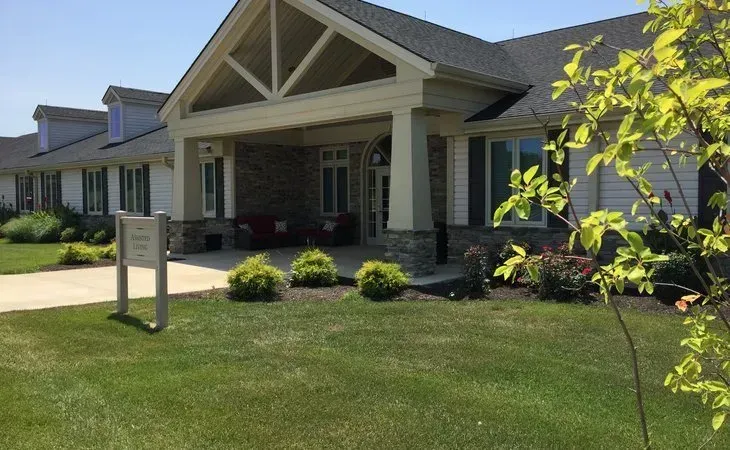 Exterior of a light-colored, single-story building with a covered entrance. Green lawn and landscaping.