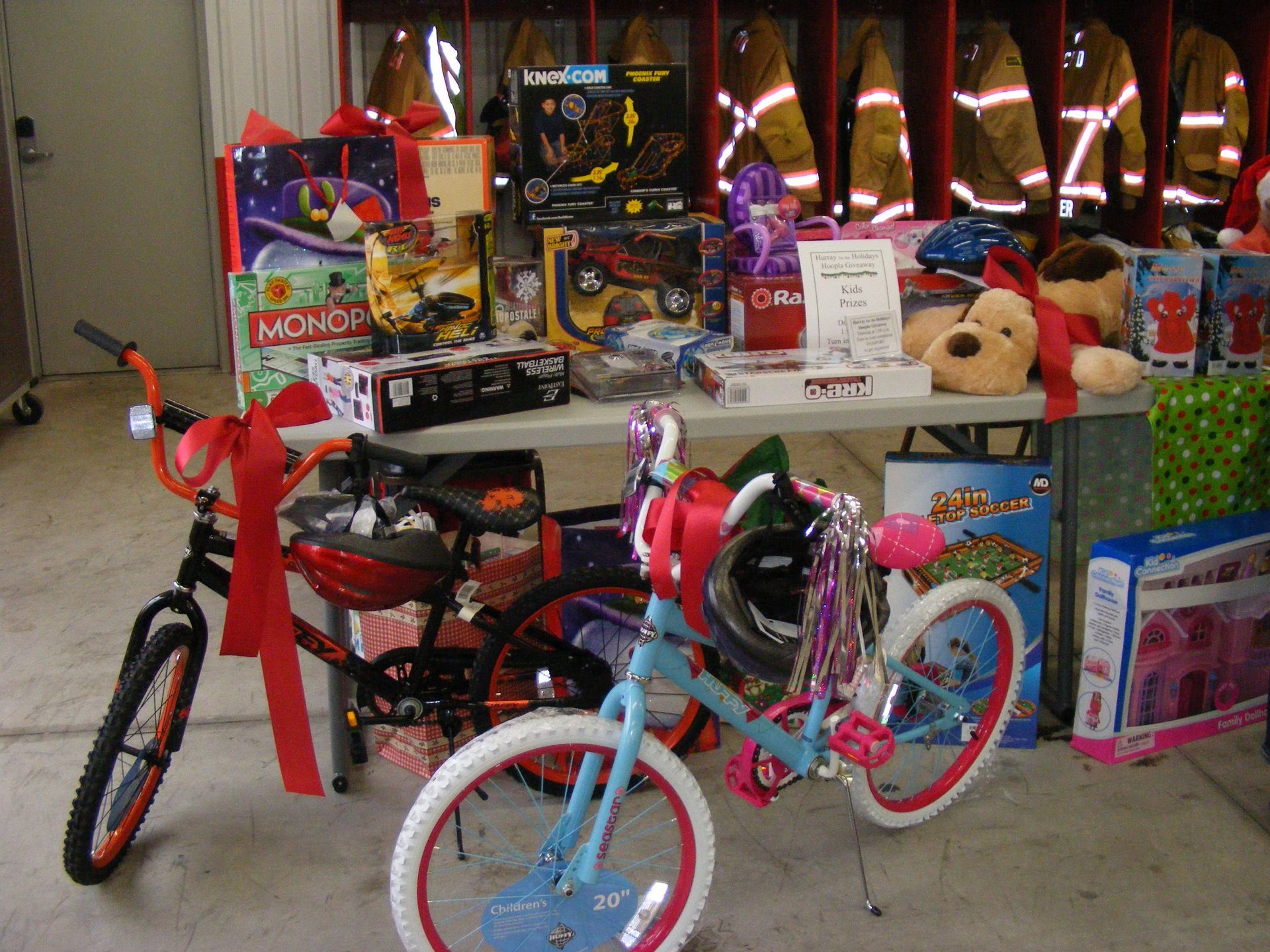 Gifts including bikes and toys, wrapped and ready, are displayed on a table in front of firefighter gear.