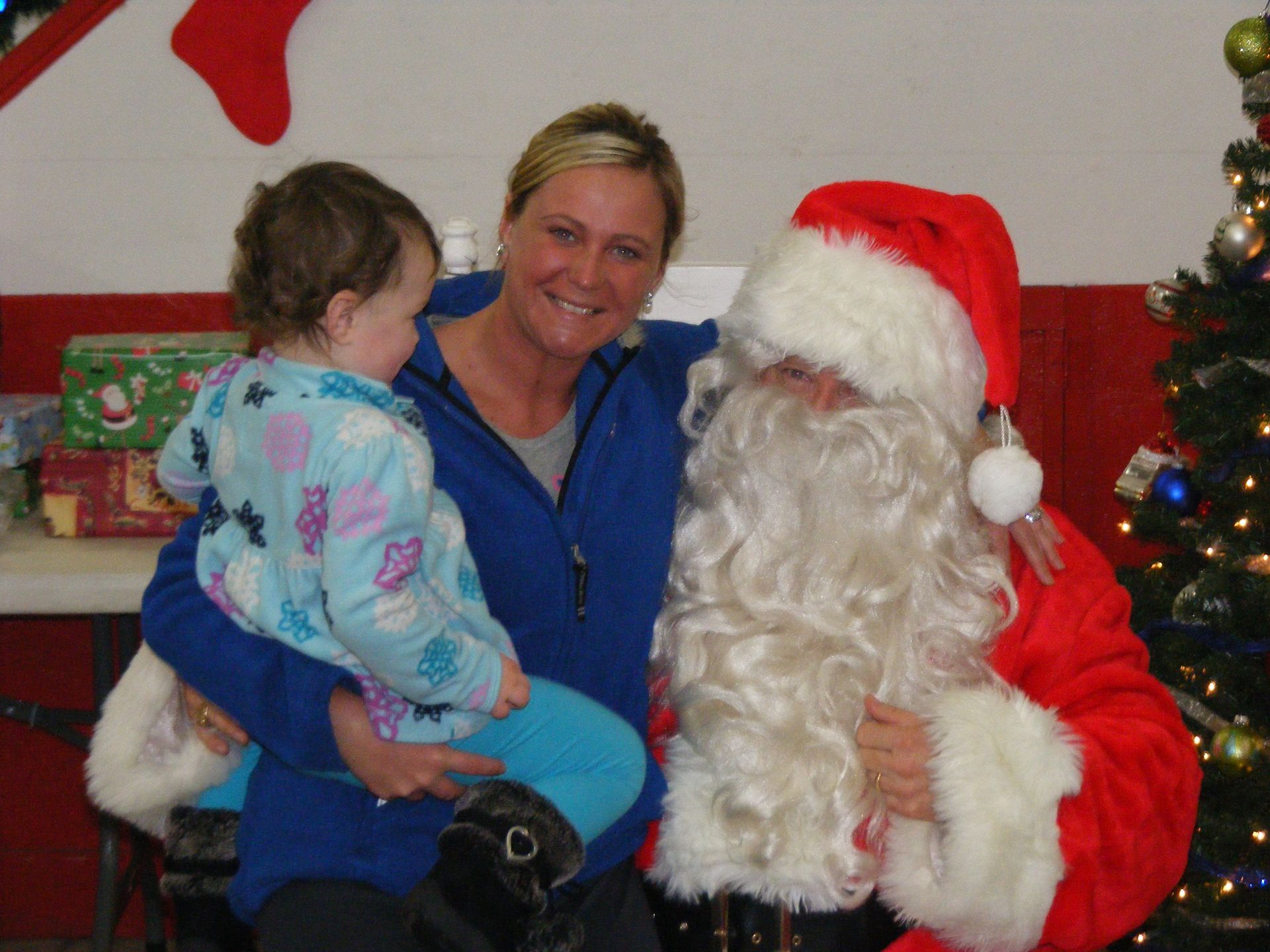 Woman and child sitting with Santa, smiling near a Christmas tree.