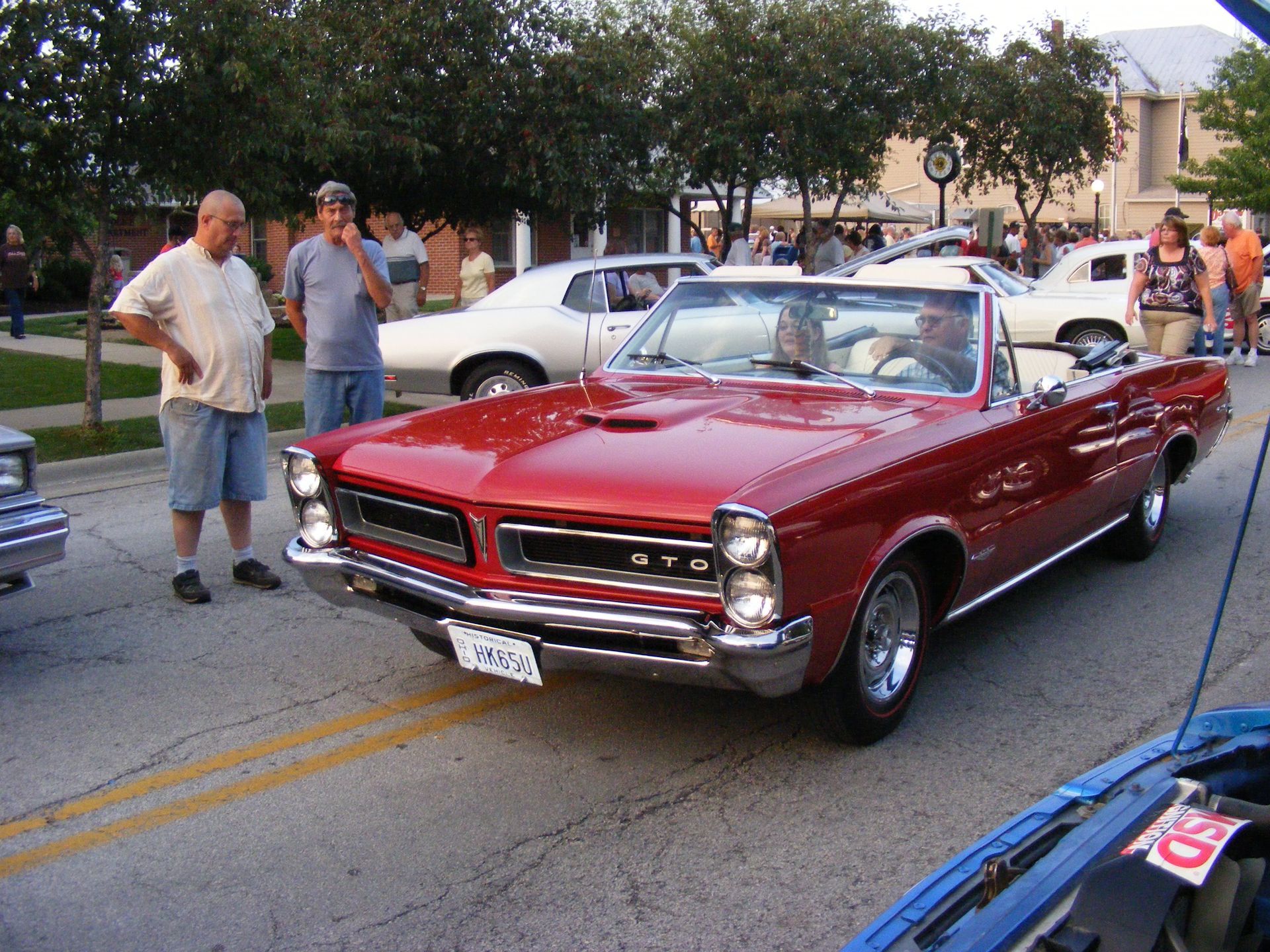Red convertible car on a street, observed by onlookers.