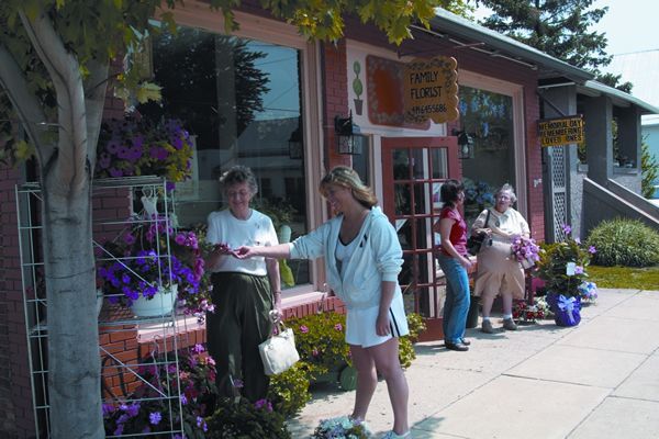 People outside a flower shop. A woman points at flowers held by another person. Others walk by.