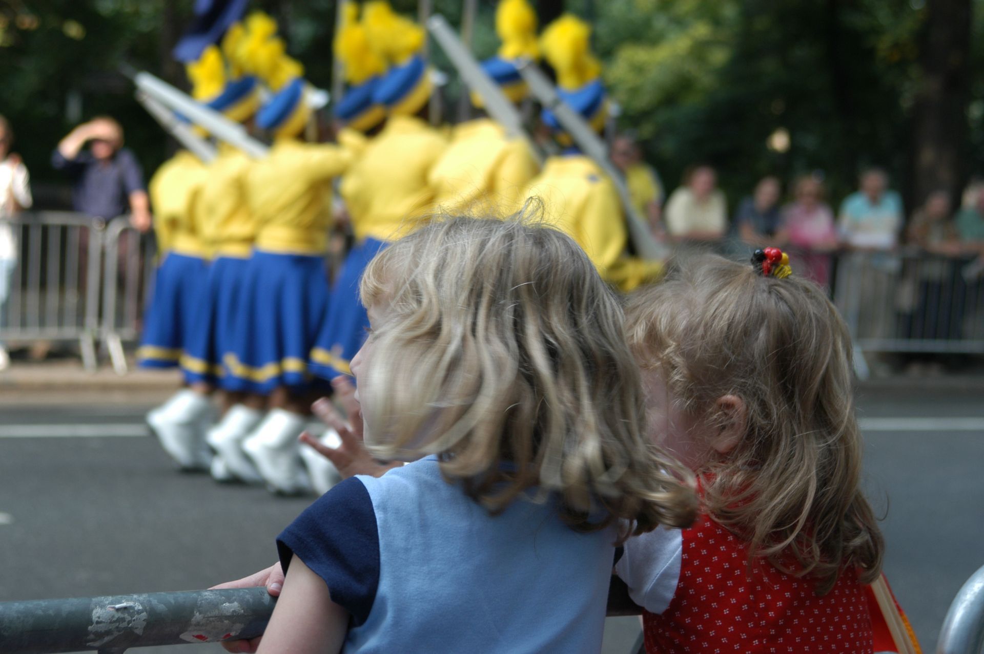 Two young children watching a marching band parade with yellow and blue uniforms.