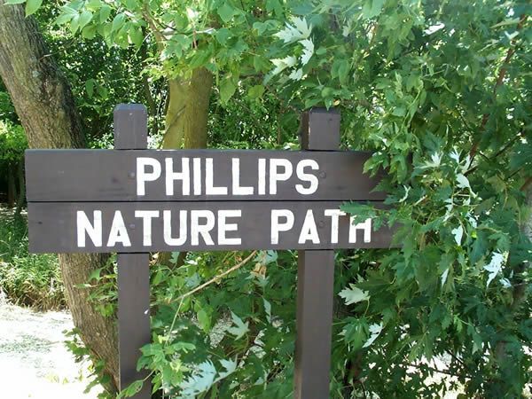Wooden sign for Phillips Nature Path in a leafy green setting.