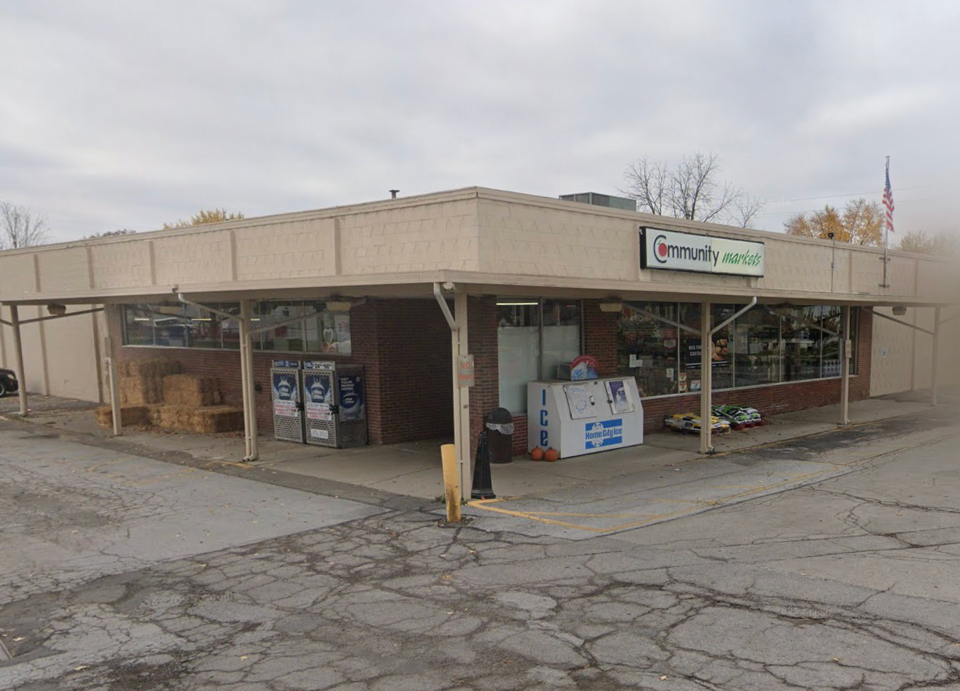 Corner store with tan awning, brick facade, and open windows. American flag flies.