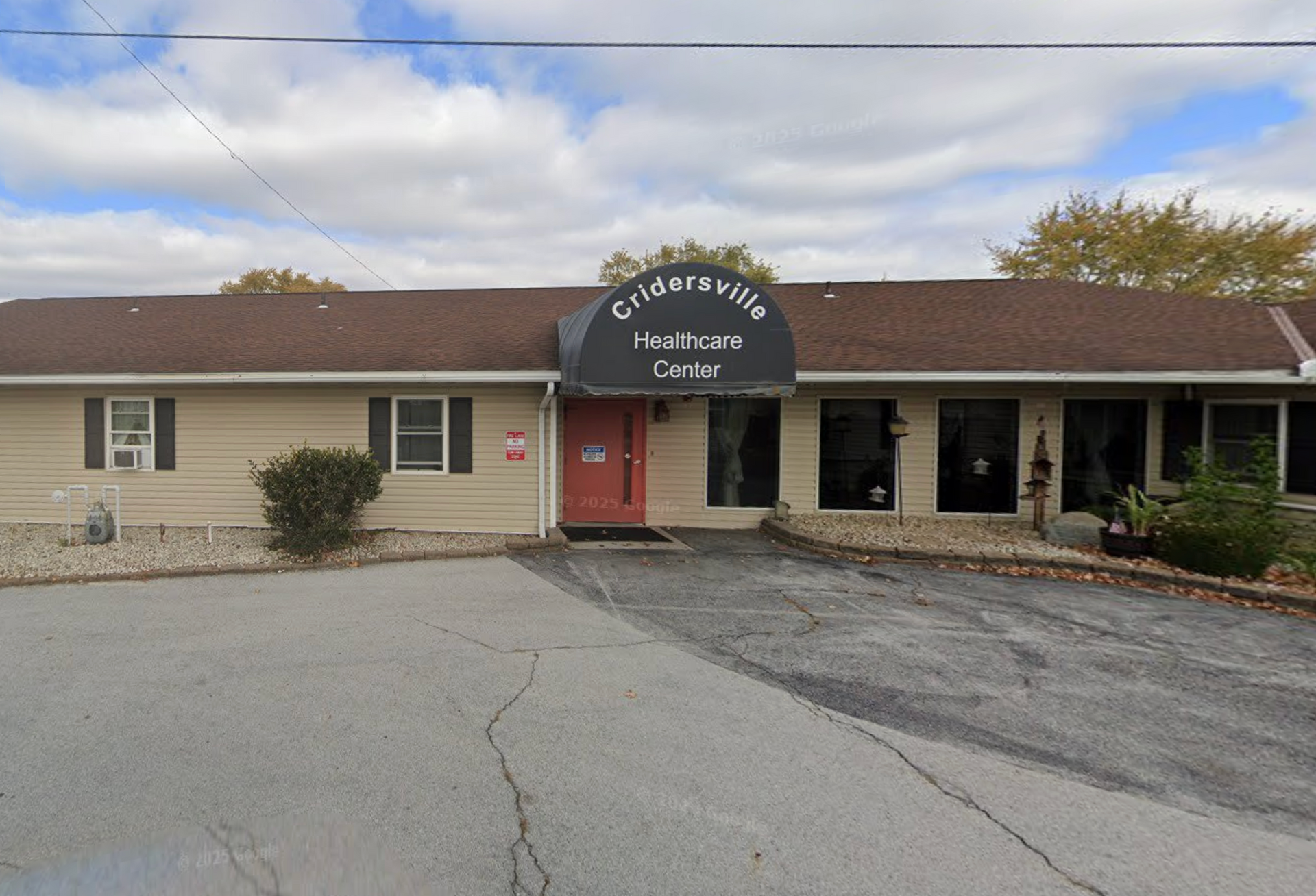 Exterior of the Cristoville Healthcare Center, tan building with a black awning and red door.
