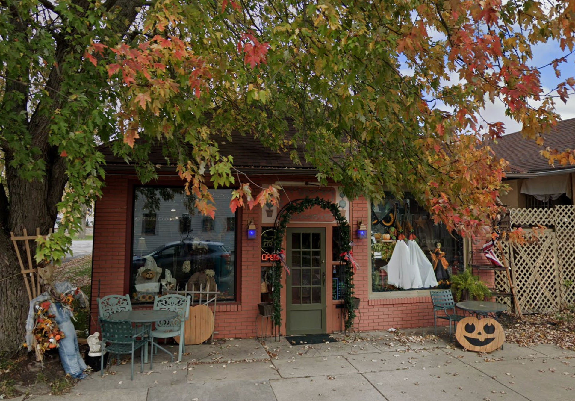 Red brick shop with Halloween decorations under a tree with autumn leaves.