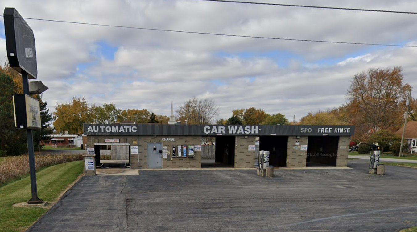 Exterior of an automatic car wash with open bays and a sign. Dark pavement. Cloudy sky.