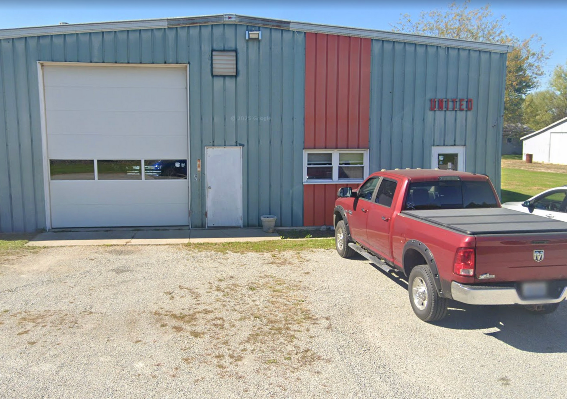Red pickup truck parked in front of a blue and red metal building.