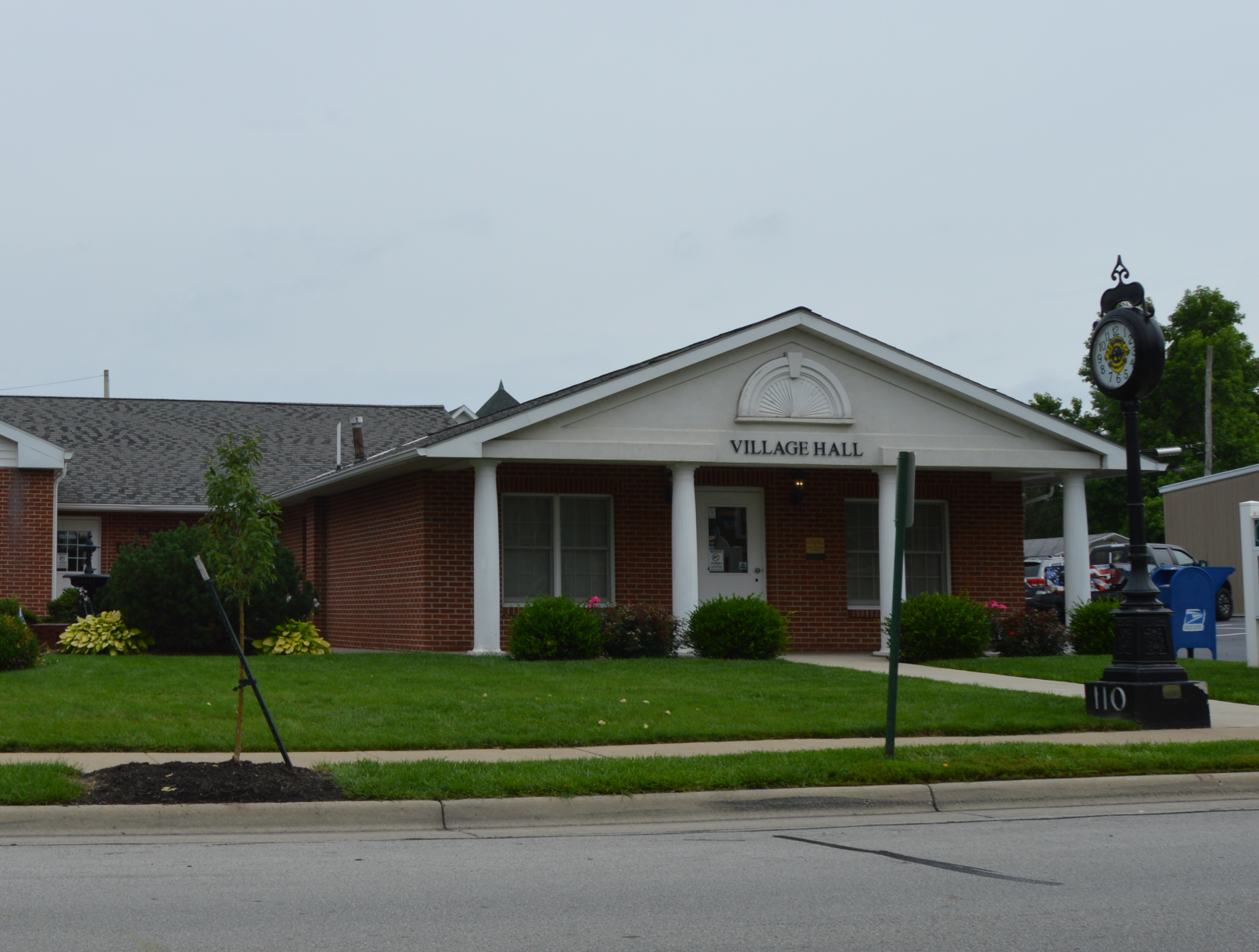 Village Hall, a one-story brick building with a white porch and clock tower.