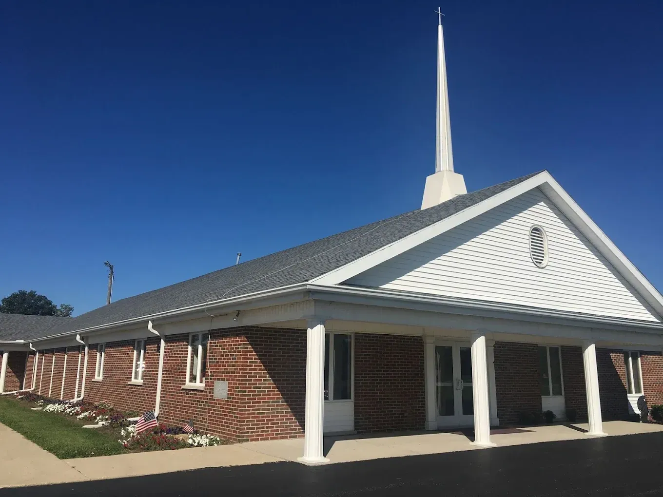 Church building with a white steeple, red brick facade, and blue sky.