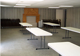 Empty room with white tables and chairs, a faux fireplace, and a door.