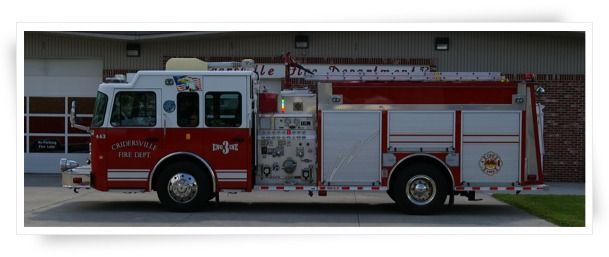 Fire truck in front of a building. It's red and white, parked in a parking lot.