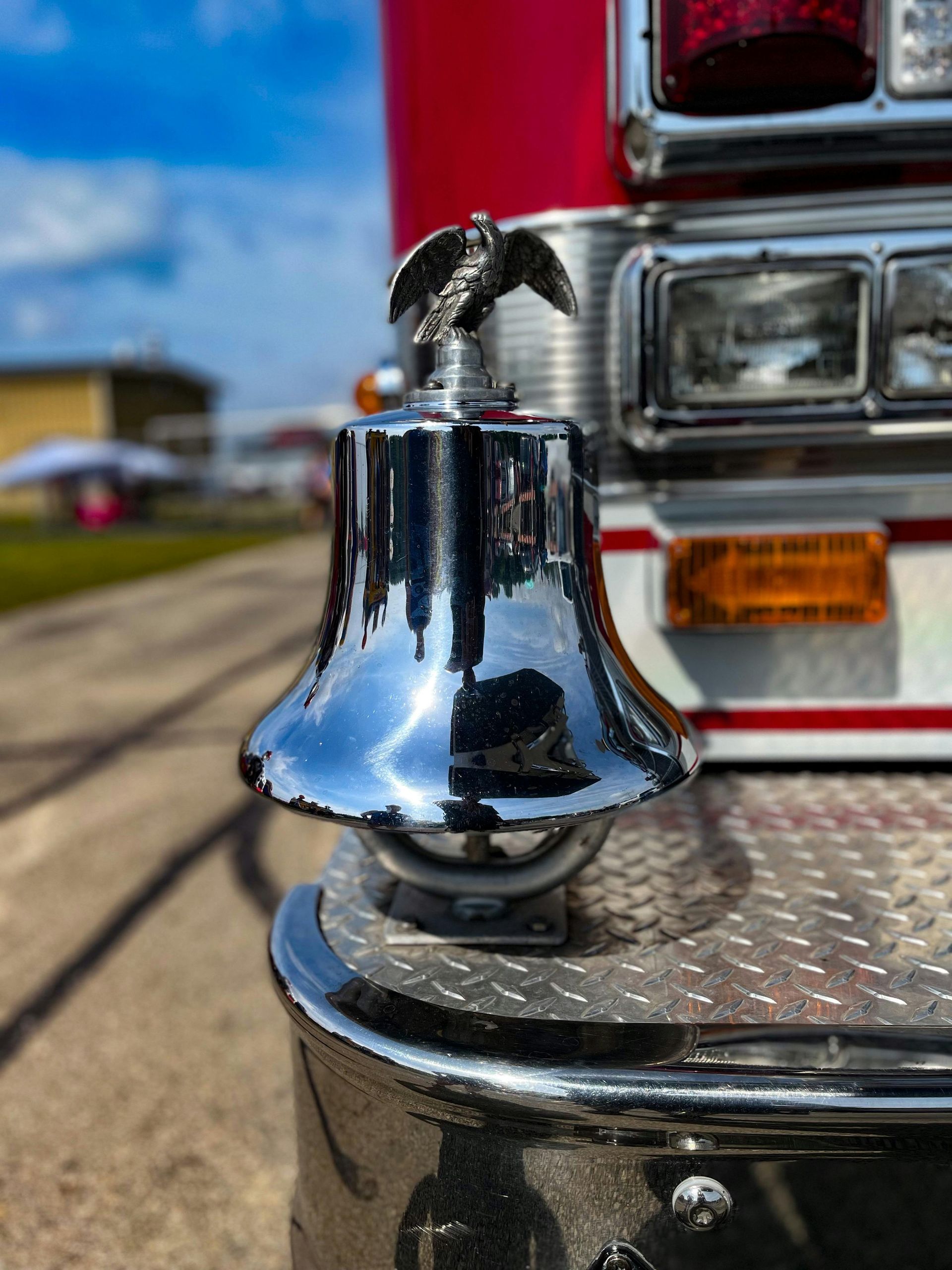 Shiny chrome fire truck bell with a silver eagle on top, close-up. Reflects surroundings.