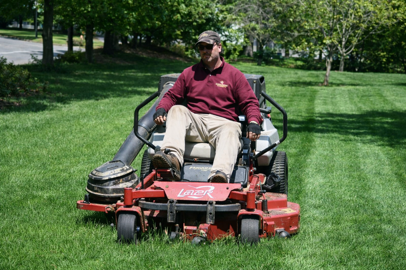 Man mowing a green lawn on a red riding mower in a park.
