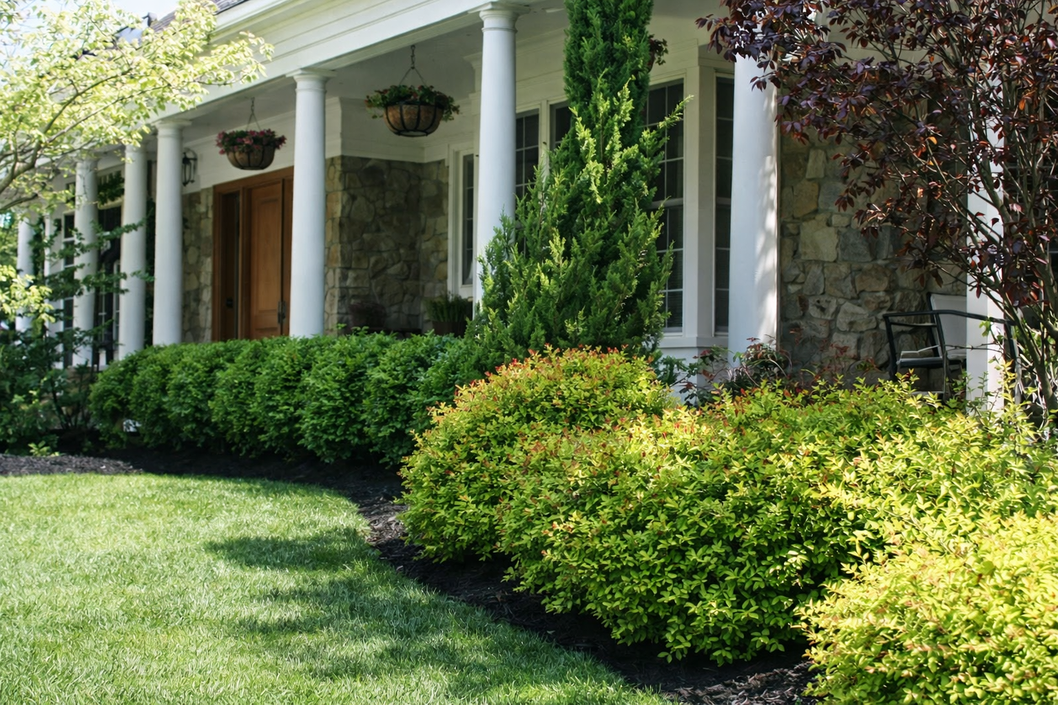 White-columned house porch with lush green shrubs and lawn in front