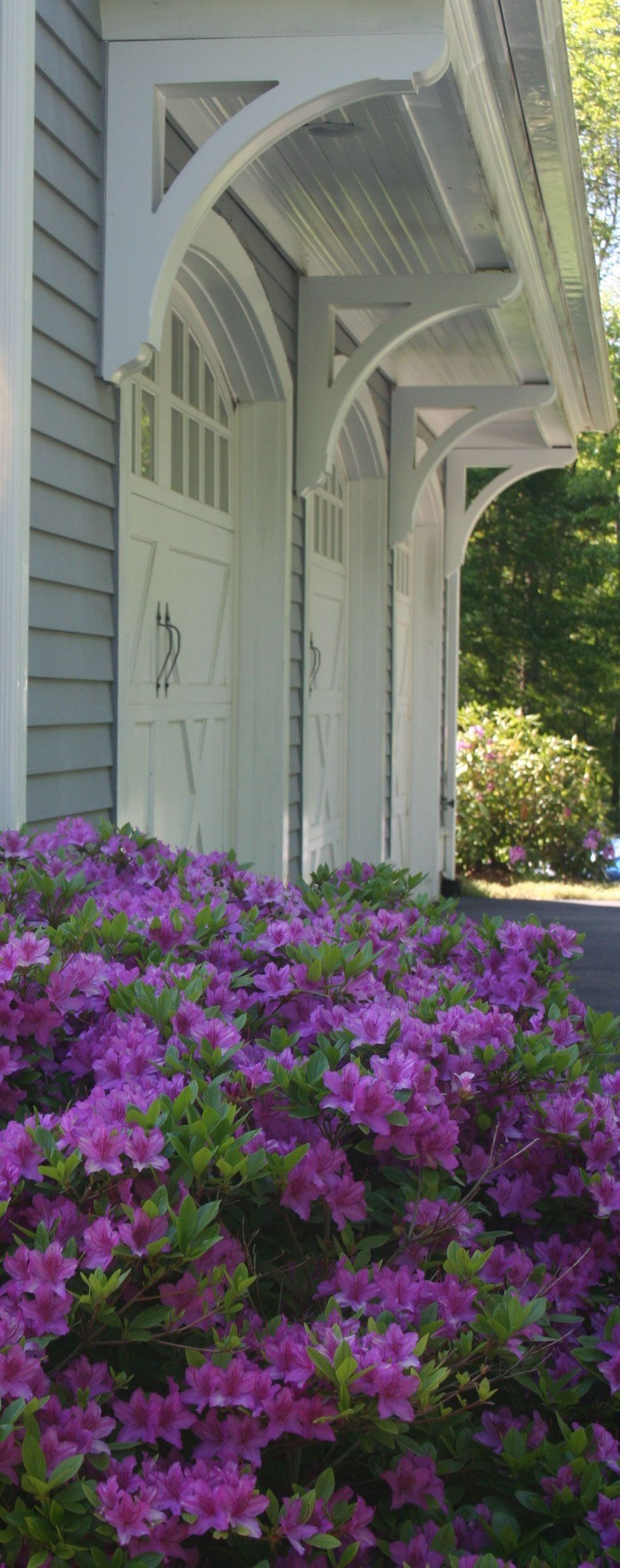 White porch with hanging beams beside blooming purple flowers and sunlit greenery