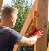 Person in red gloves using a level to align a wooden post outdoors.