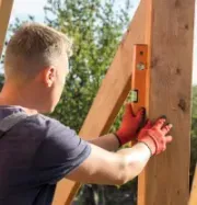 Person in red gloves using a level to align a wooden post outdoors.
