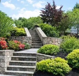 Stone steps and a landscaped garden with shrubs, flowers, and retaining walls in front of a house