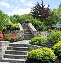Stone steps and a landscaped garden with shrubs, flowers, and retaining walls in front of a house
