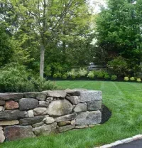 Stone wall edging a green lawn with trees and shrubs in a landscaped yard