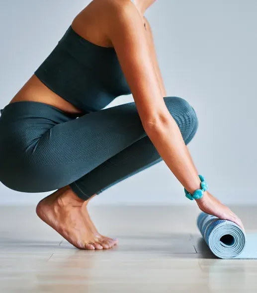 A woman is squatting down next to a yoga mat
