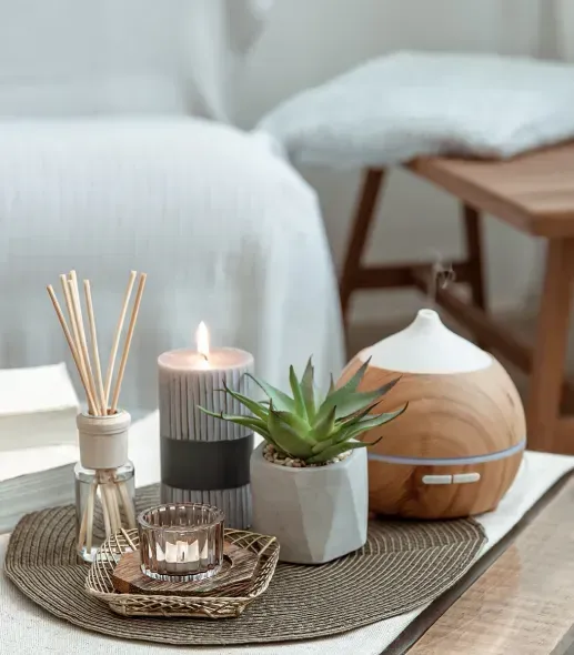 A table with candles , a plant , and a diffuser on it.