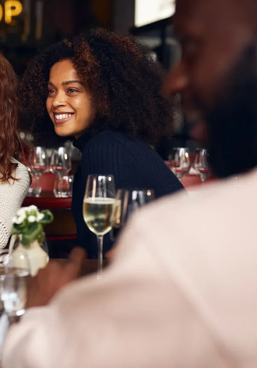 A woman is smiling while sitting at a table with glasses of wine.