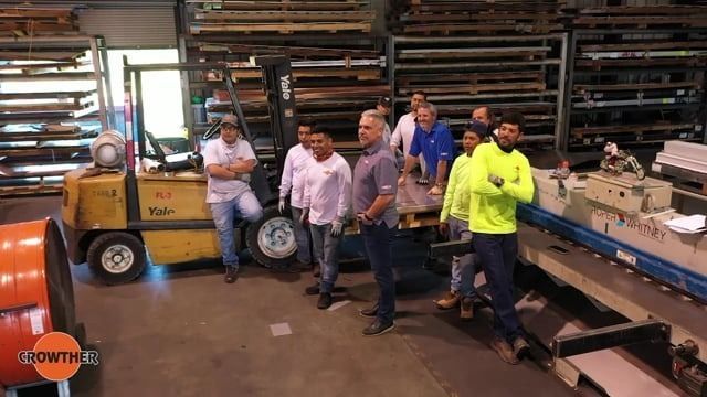 Workers standing in a warehouse beside stacked materials and a forklift