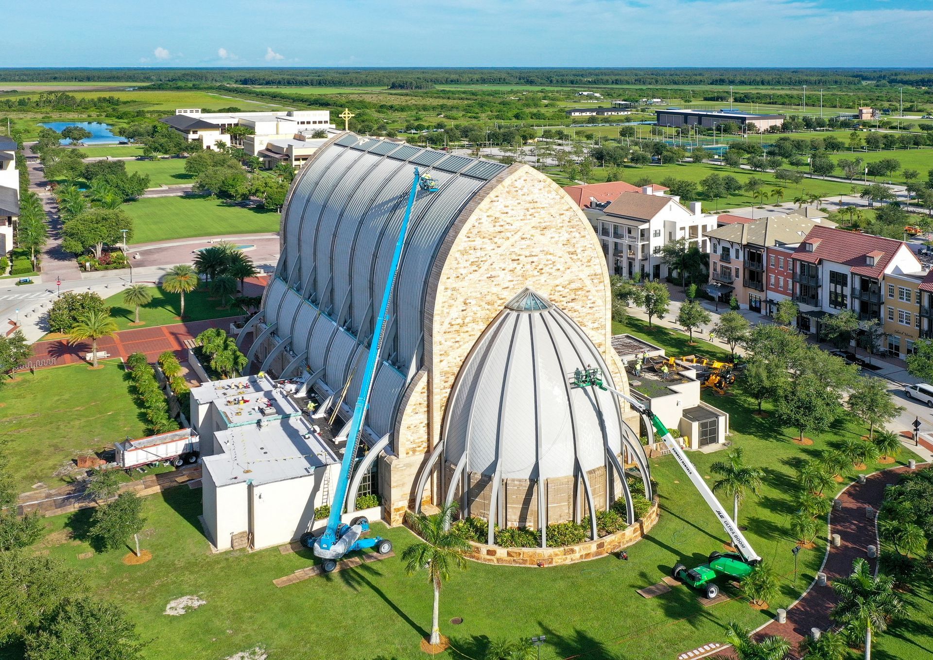 Worker installing metal roofing on a house roof, kneeling with a nail gun under a blue sky