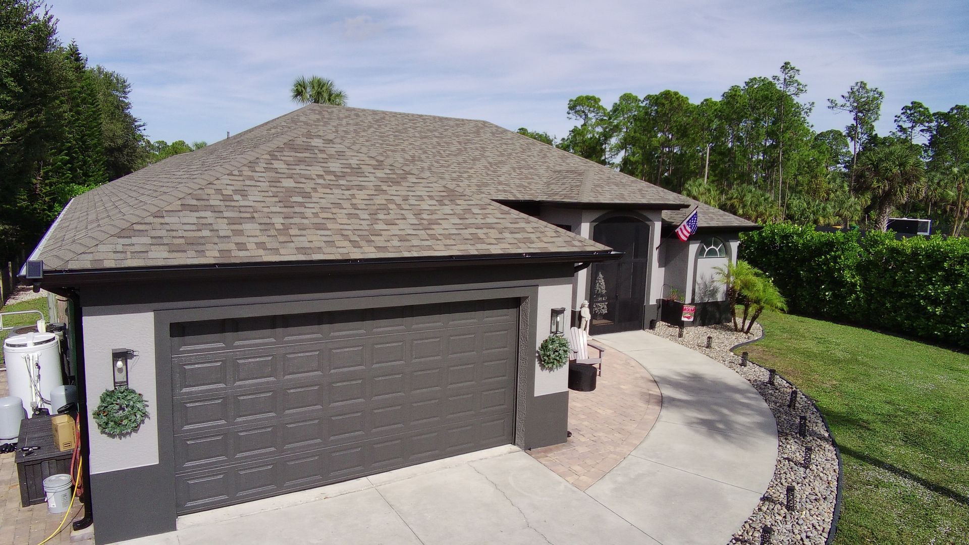 Brown suburban house with a garage, curved driveway, and landscaped front yard under a clear sky