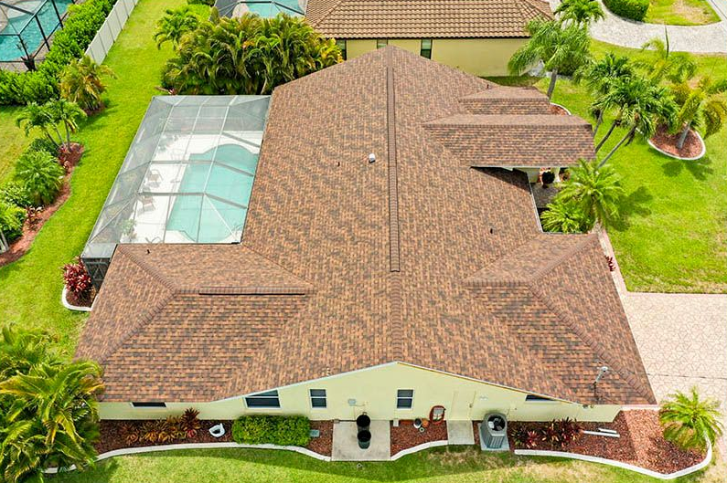 Aerial view of a tan-roofed suburban house with a screened pool and landscaped yard