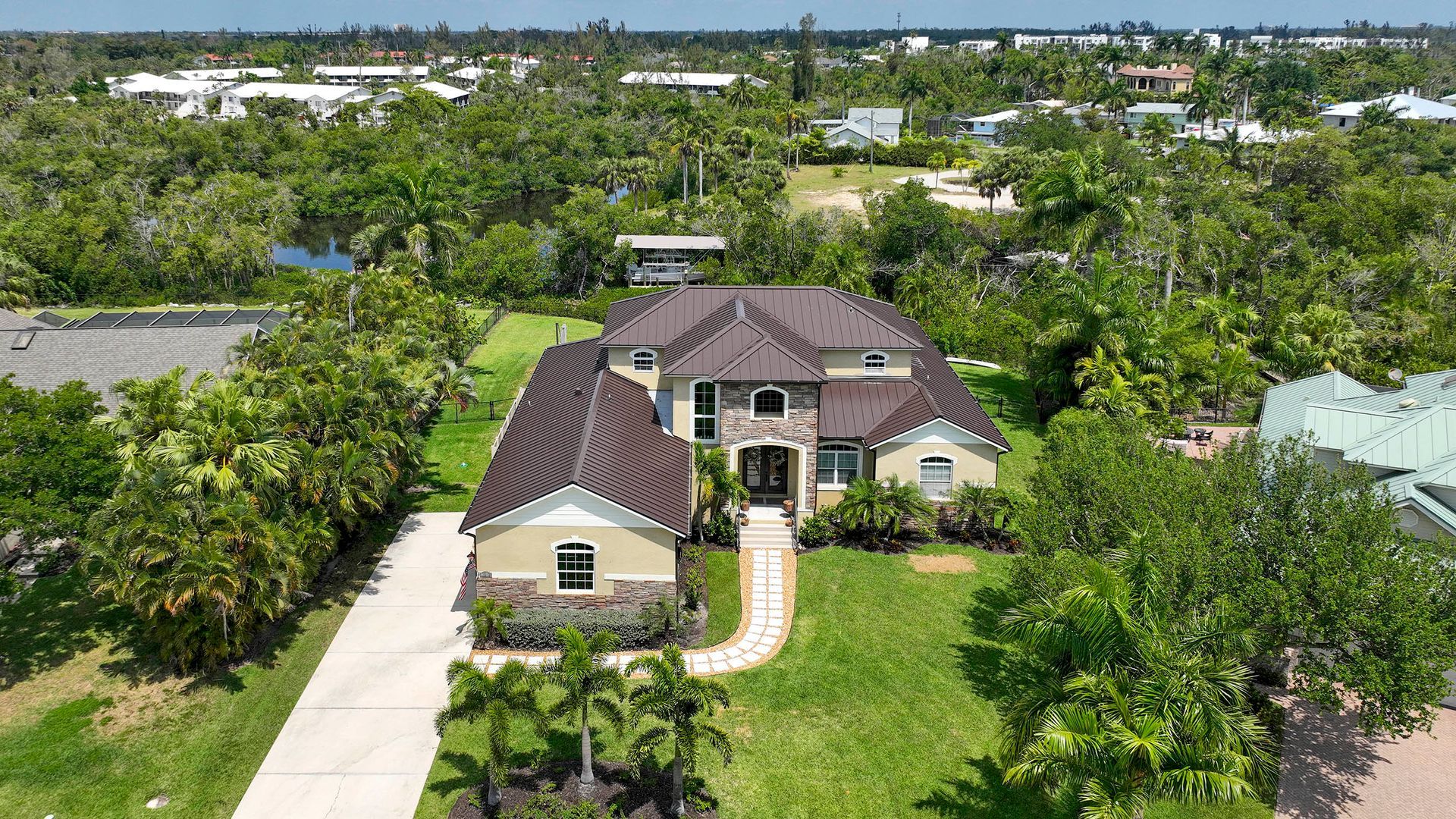 Aerial view of a beige house with a brown roof, surrounded by trees and a curved driveway.