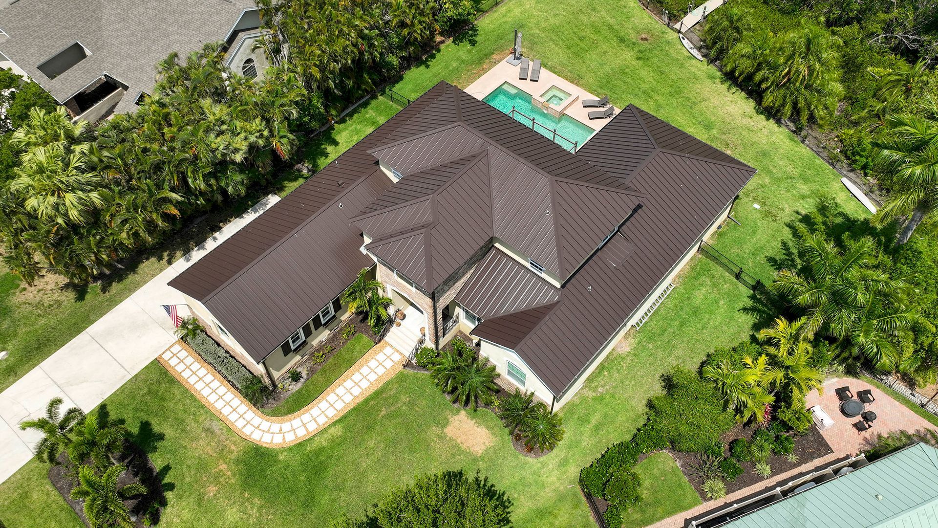Aerial view of a modern house with a dark roof, pool, and lush green landscaping.